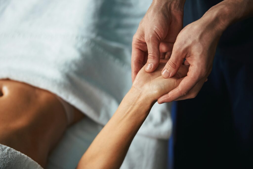 Experienced unrecognized man masseur holding patient hand in spa salon