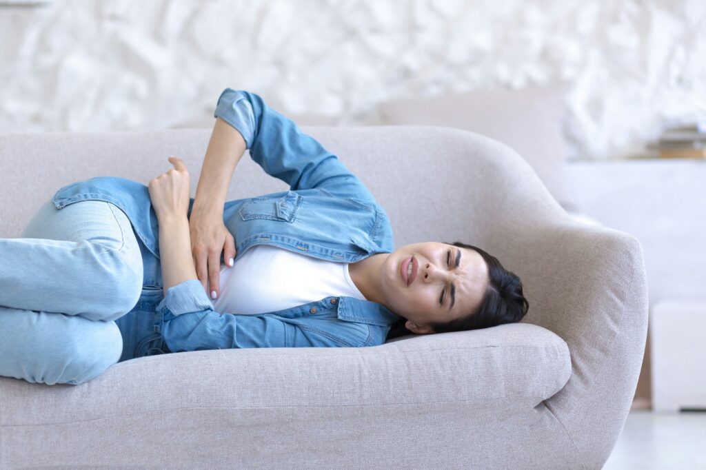 Menstrual pain. Young woman is lying on the sofa at home and holding her stomach